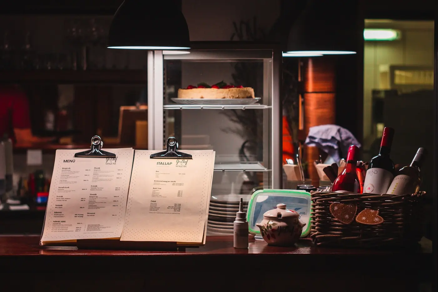 Comptoir d'un café en fin de service, deux menus sur pinces posés devant la vitrine à gâteaux