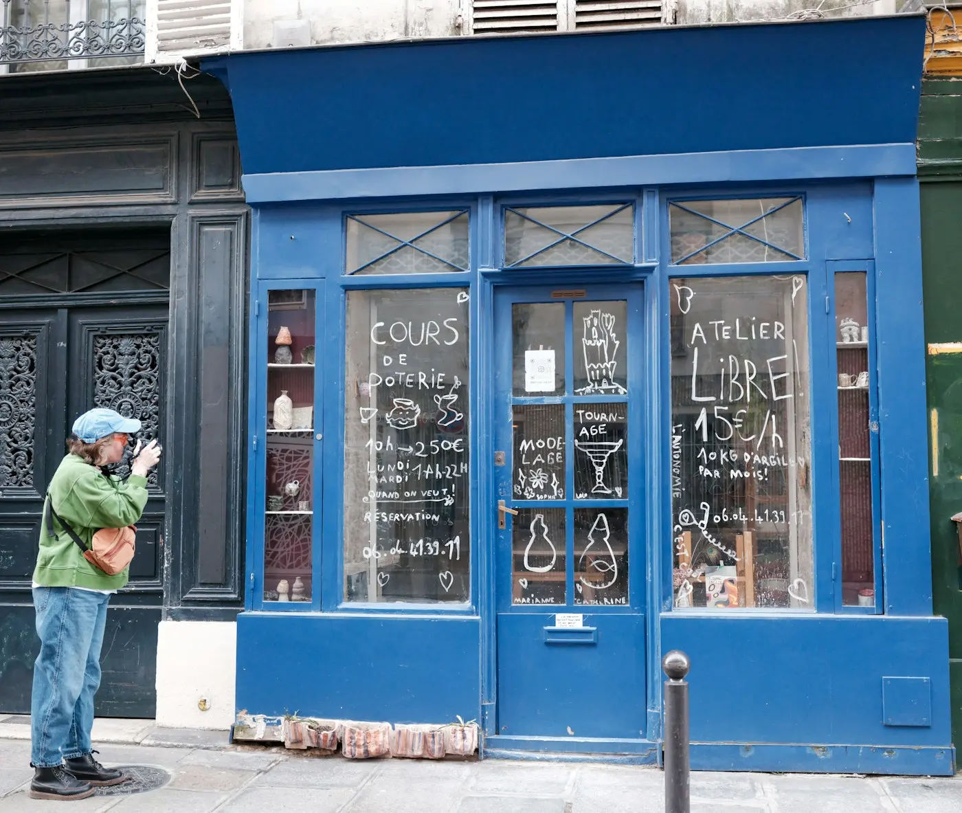 Une passante photographie avec son téléphone la devanture bleue d'un petit atelier de poterie