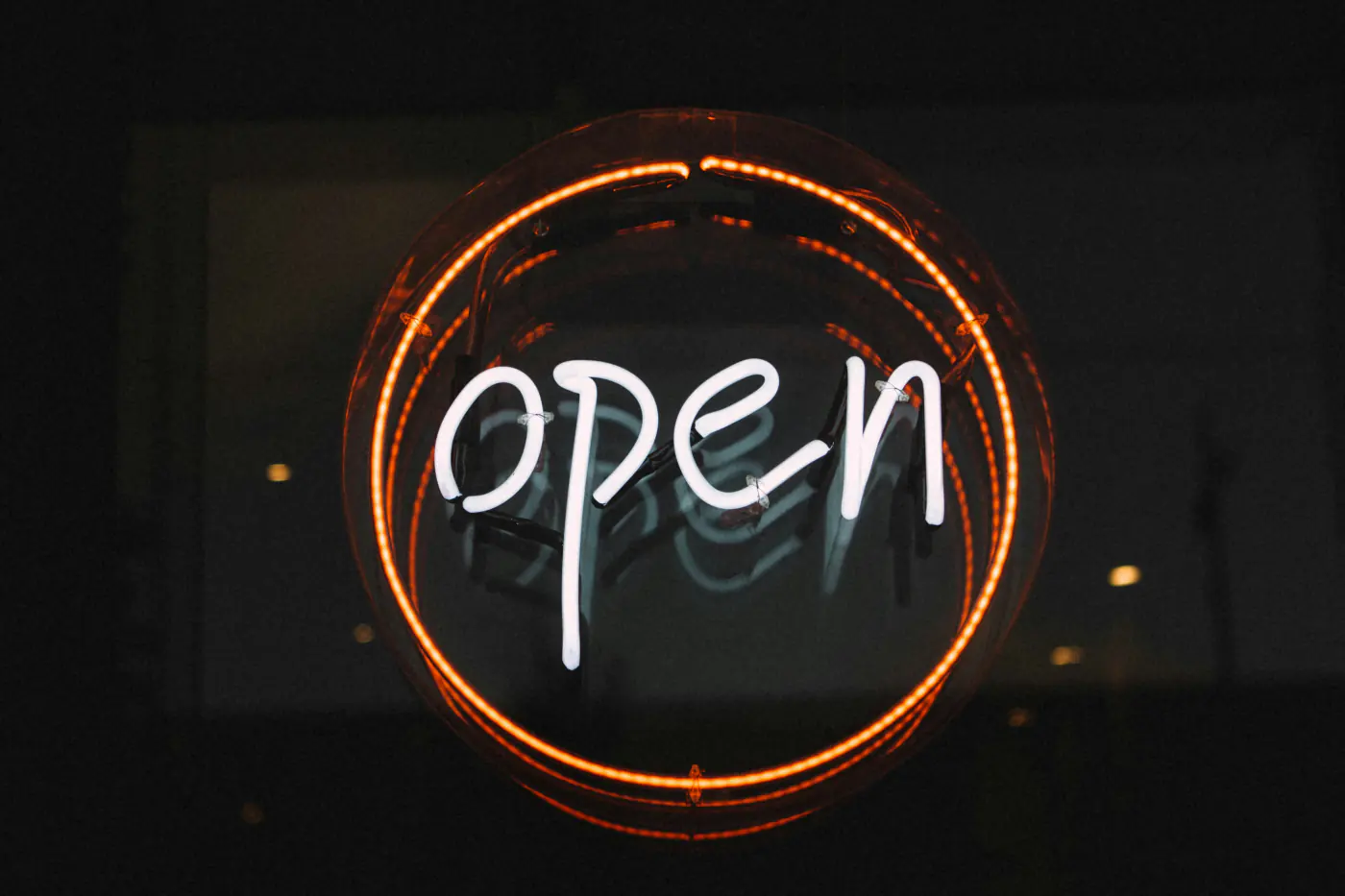 Enseigne « open » en néon blanc cerclé d'orange, allumée dans la vitrine d'un commerce la nuit