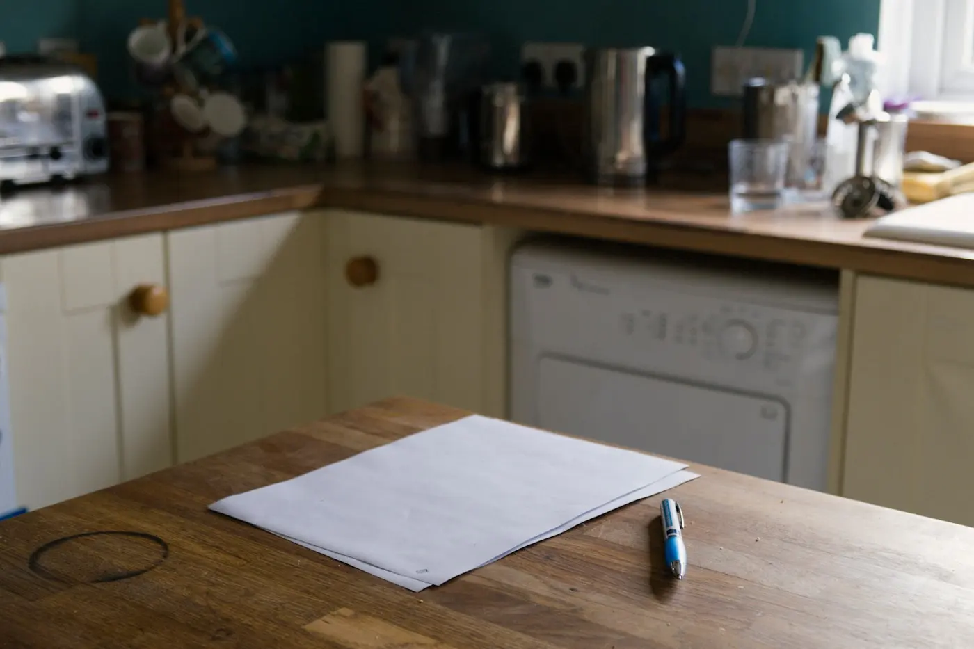 Feuille de papier vierge et stylo posés sur une table en bois dans une cuisine