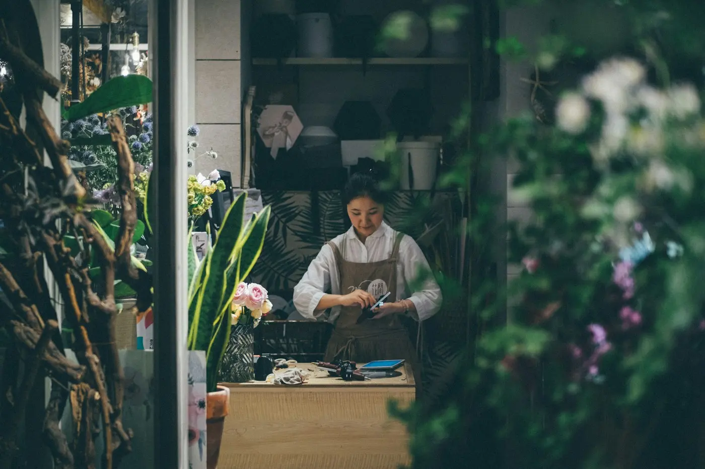 Une fleuriste consulte son téléphone derrière le comptoir de sa boutique, entre les plantes